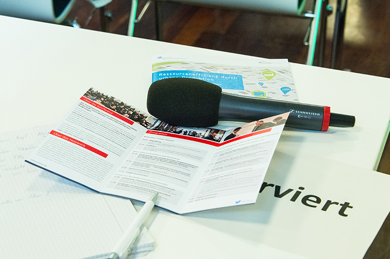 Das Bild zeigt ein Mikrofon, einen Notizblock, einen Stift und zwei Flyer zu einer NeRess-Veranstaltung.